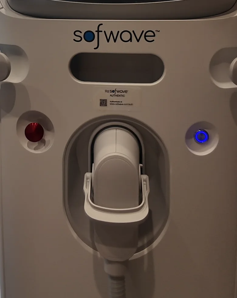 Front of a Sofwave treatment console showing the Sofwave name, a red and a blue indicator light and the handpiece resting in its cradle
