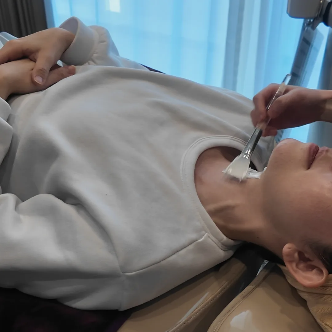Cream being brushed onto the neck and jawline of a person lying back on a treatment chair