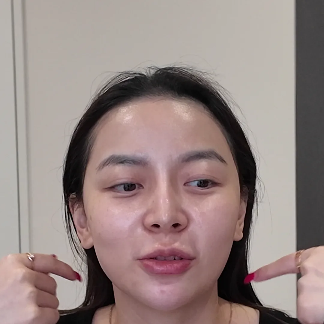 크림을 바르지 않은 사람이 카메라를 보며 두 검지로 뺨과 턱선 쪽을 가리키는 모습