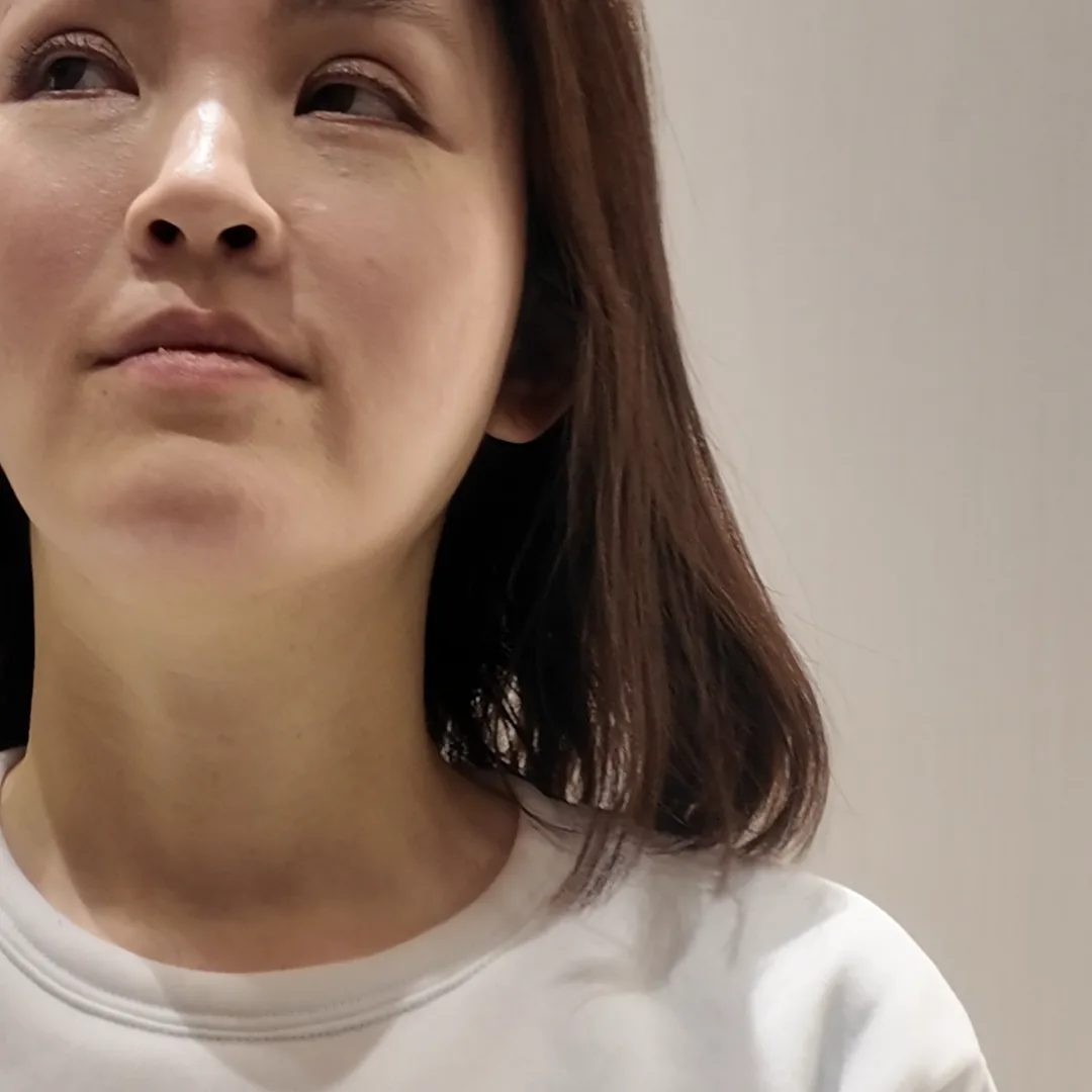 A person in a white sweatshirt standing against a plain wall and looking to the side
